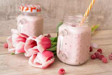 Berry mix protein smoothies in mason jar on light background with tulips flowers, spring healthy lifestyle concept