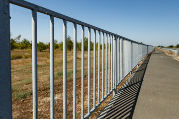 metal fence between the field and the pedestrian walkway on the highway.