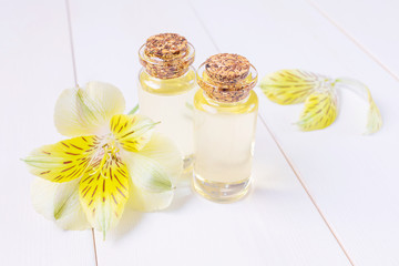 The concept of aromatherapy, spa. Bottles with floral essential oil on a white wooden background. Nearby is a yellow flower. Cozy still life in bright colors.