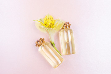 The concept of aromatherapy, spa. Bottles with floral essential oil and a yellow flower on a pastel pink background. Cozy flat lay in bright colors. Copyspace, minimalism, top view.