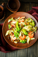 Fresh salad plate with shrimp, penna pasta, avocado and arugula on wooden background flat lay. Healthy food.