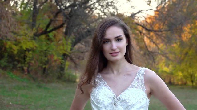 Young brunette woman in long white dress walks along autumn colorful forest.