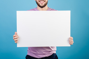 smiling man holding white copy space paper isolated on blue background