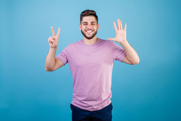 Fototapeta premium smiling man showing seven fingers isolated on blue background