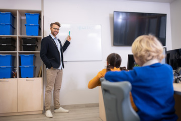 Male teacher standing at whiteboard, explaining progamming to pupils