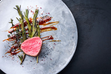 Barbecue dry aged beef fillet medallion steak natural with fried herbs and spice as top view on a modern design plate with copy space right
