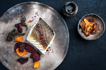 Gourmet fried European skrei cod fish filet with algae and vegetable crisps as top view on a modern...