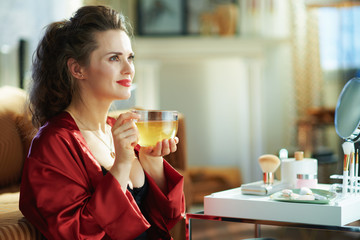 pensive woman with cup of tea at modern home in sunny day