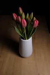 Red tulips flower bouquet on a white pot on a wooden surface isolated on a black background