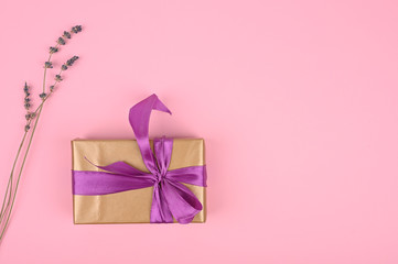 Festive arrangement: box with gift, ribbon and flowers lie on a pink table, top view