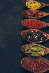Colorful various spices in wooden spoons on old dark background. Top view with free space