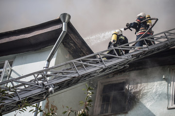Firefighters on ladders in oxygen masks extinguish the fire in an old house in the middle of the...