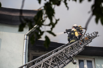 Firefighters on ladders in oxygen masks extinguish the fire in an old house in the middle of the city