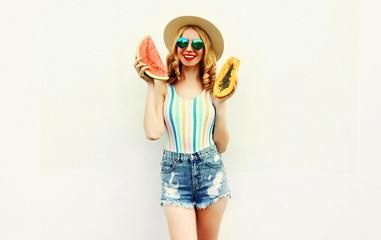 Summer portrait attractive smiling woman with slice of watermelon and papaya wearing straw hat, sunglasses, shorts over white background