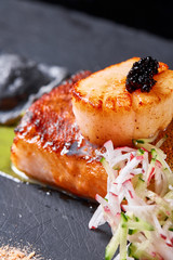 Scallops and ravioli. Seafood, pike perch fish, caviar and black dumplings in a plate on a dark table close-up. Healthy food.