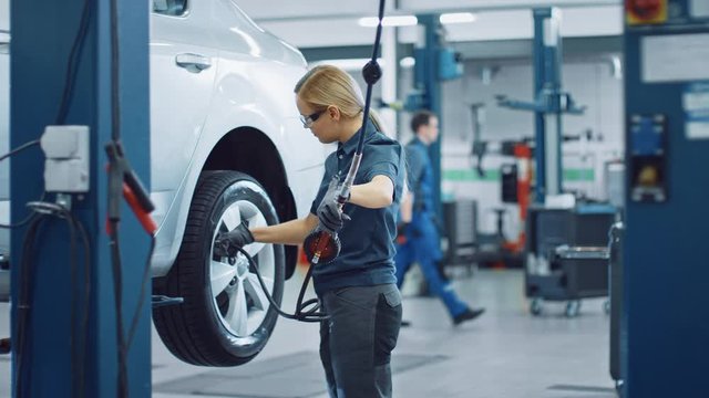 Blond Female Mechanic is Checing the Tire Pressure in a Wheel of a Vehicle. Empowering Woman Works in a Modern Clean Car Service. Specialists Inflates the Wheel After Fixing a Component on a Vehicle.