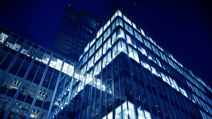 Fototapeta premium Night architecture - building with glass facade.Blue color of night lights. Modern building in business district. Concept of economics, financial. Photo of commercial office building exterior. Abstra