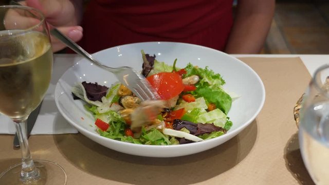 Woman eat fresh seafood salad at Spanish restaurant, part of set menu for lunch. Green lettuce leaves and red tomato slices, small mussel and other sea products, seasoned with olive oil