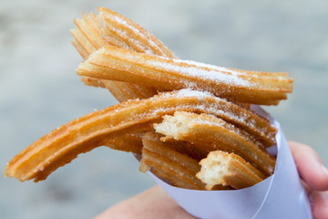 Churros sprinkled with sugar held in a paper cone by a caucasian hand. Tasty, typical, fried Cuban street food. Close up background sweet dough snack.