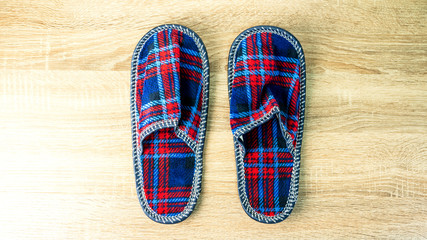A pair of colorful comfortable, cushioned, checkered disposable slippers are on the wooden floor. Close-up.