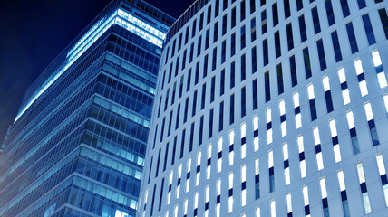 Night architecture - building with glass facade.Blue color of night lights. Modern building in  business district. Concept of economics, financial. Photo of commercial office building exterior. Abstra