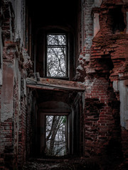 Fototapeta na wymiar Inside of the mansion ruins. Red brick walls and empty window holes on two floors. Dark empty space of the ancient dilapidated building. Gloomy symbol of desolation and forsaken.