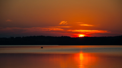 warm summer red-orange sunset over the lake and sun disc behind the forest