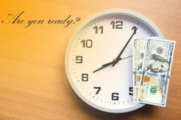 Analog clock and dollars on a wooden background. Banknotes are on the clock and next. Macro. Top and side view. The clock is 20:05, 08:05.  Copy Space