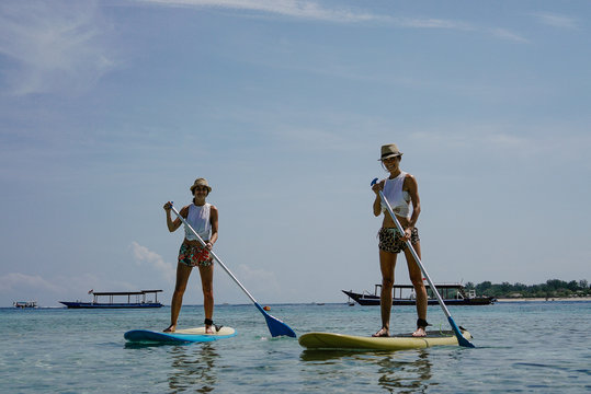 Girls Friends Surf On Paddle Board On Sea 