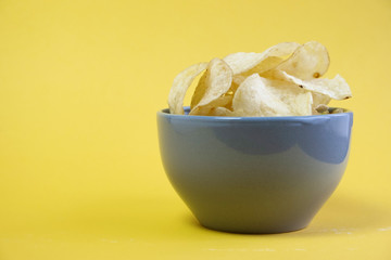 Ceramic gray cup, a bowl full of chips stands on a yellow background. Snack for beer. Unhealthy food. Place for text
