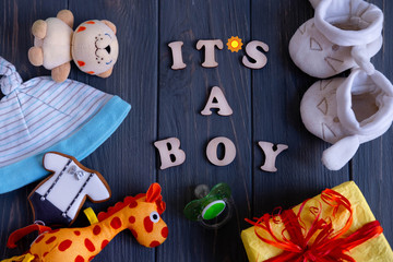 This is a boy. Greeting card with an inscription of wooden letters with toys for newborns, a box with a gift on a gray dark wooden background. Greeting card for newborns in dark colors.