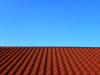 Red tile roof under blue sky. The photo is divided in half. One part is a roof made of clay tiles and the other is a pure blue sky.