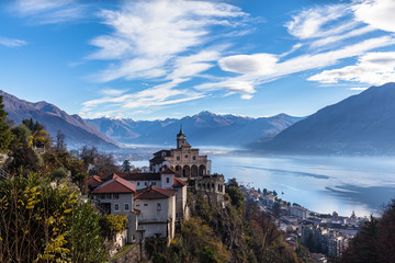 Fototapeta na wymiar Stunning aerial panorama view of Madonna del Sasso church above Locarno city with Lake Maggiore, snow covered Swiss Alps mountain peaks and blue sky cloud in background in autumn, Ticino, Switzerland