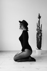 Beautiful girl in a black bodysuit and a black hat on her knees