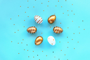 Painted gold and white eggs on a blue background with confetti. Easter concept. Top view, flat lay.
