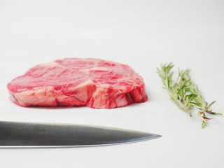 Raw uncooked fresh rib eye beef steak and rosemary and kinfe blade on white background.