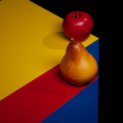 yellow pear and red apple on blue paper. Black background