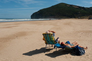 Pareja de turistas tomando el sol en la playa de Berria de Santoña, en el Camino de Santiago del Norte.