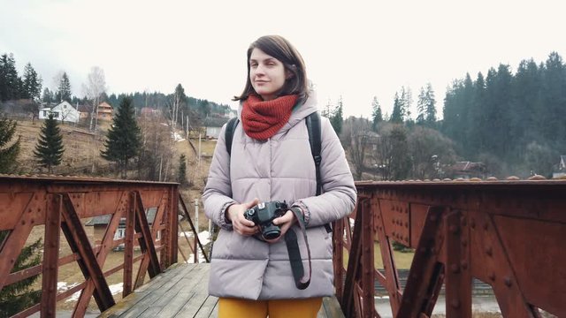 Girl taking pictures on professional camera walking in mountainous area. Female traveler stops in the middle of the bridge and takes a picture on a photo camera. 
