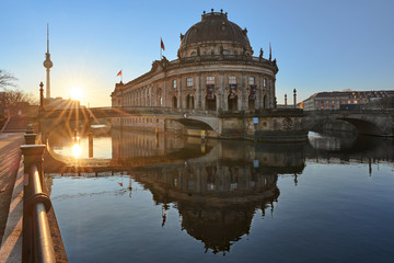 Fototapeta premium Berlin, Germany, Museum Island on Spree river and TV tower in the background at sunrise, Bode-Museum, cityscape early in the morning, reflections in the water, beautiful sun star