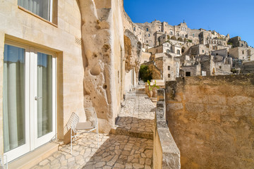 A modern sliding glass door and metal chair sit outside a patio in the ancient cave hillside city of Matera, Italy.