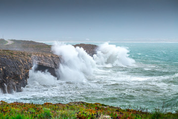A huge ocean waves breaking on the coastal cliffs in at the cloudy stormy day. Breathtaking romantic seascape of ocean coastline. Peniche, Portugal.
