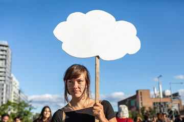 A close up portrait of a stern and serious environmental campaigner protesting on a city street, with blank thought bubble placard and copy space