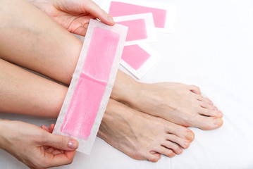 Woman using pink wax strips. Beautiful woman doing depilation for her legs with waxing, isolated on...