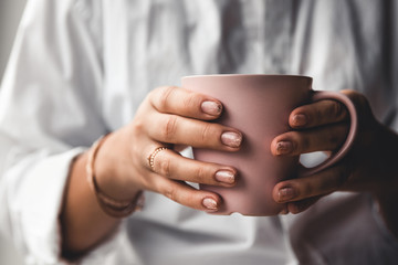 Woman in a white t-shirt holds morning coffee in a pink ceramic cup. Manicure. Front view