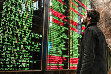 Young man looking on time table in protective mask to prevent virus with blurred image of display