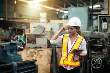 Female industrial engineer wearing a white helmet while standing in a heavy industrial factory...