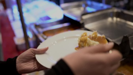 This video shows anonymous female hands adding gravy to fresh delicious mashed potatoes to her plate at a buffet.