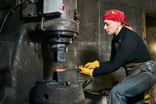 woman metal artist processes a hot workpiece with a power hammer - Powered by Adobe