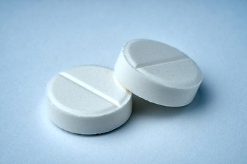 Closeup of two white tablets on a white background with texture.